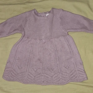 stickad klänning från Newbie - Supersöt ljuslila stickad klänning från Newbie i storlek 56. Klänningen har lång ärm, fina hjärtformade detaljer och mönster nertill samt knappar i trä på ryggen. Perfekt för dig som gillar mjuka material och gulliga detaljer.