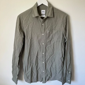 Olivgrön skjorta från Zara i linneblandning - Olivgrön skjorta från Zara i en skön blandning av bomull och linne. Klassisk krage, bröstficka och vita knappar framtill. Långärmad och med enkel, stilren design som funkar till många olika looks. A9Af