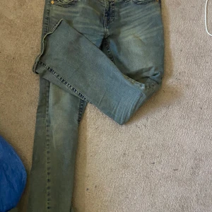 True Religion Joey Low Rise Flare Jeans - Säljer ett par blå jeans från True Religion, modell Joey Low Rise Flare. De har låg midja och utsvängda ben, klassisk femficksdesign och snygga kontrastsömmar. Bakfickan har lock och knapp med märkets logga. Perfekta för dig som gillar en retro vibe.