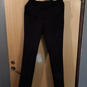 Svarta kostymbyxor från BikBok - Snygga svarta kostymbyxor från BikBok i storlek 36. Byxorna har en klassisk rak passform med hällor för bälte och diskreta fickor framtill. Perfekta för en clean och stilren look.