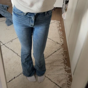 Blå bootcut jeans med hög midja - Säljer ett par klassiska blå jeans med bootcut-modell och hög midja. Jeansen har fem fickor, dragkedja och knapp framtill. Tillverkade i mjukt denimtyg som sitter snyggt över höfterna och släpper ut vid bensluten. Perfekta för en chill och trendig look.