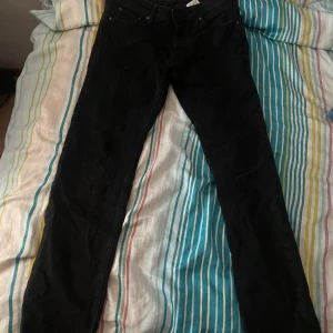 Svarta jeans från Jack & Jones tapered Mike storlek 29:32 - Svarta jeans från Jack & Jones med klassisk femficksdesign och rak passform. Byxorna är tillverkade i bomull och har en stilren look som funkar till många olika outfits. Perfekt för dig som gillar enkel och snygg stil.