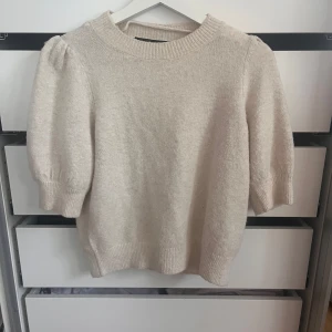 Beige stickad tröja Vero Moda - Säljer en beige stickad tröja från Vero Moda i storlek XS. Tröjan har puffade korta ärmar och bred ribbad kant vid hals, ärmslut och nederkant. Perfekt för dig som gillar en enkel men ändå trendig look med lite volym på axlarna.
