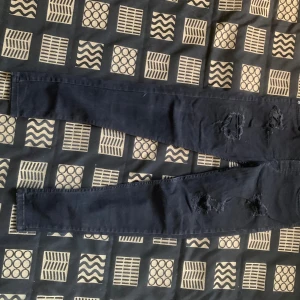 Svarta skinny jeans med slitningar - Säljer ett par svarta skinny jeans från Denim Jeans med snygga slitningar på båda benen. Jeansen har klassisk femficksdesign och smal passform som sitter tajt längs benen. Perfekta för dig som gillar en edgy och trendig look.