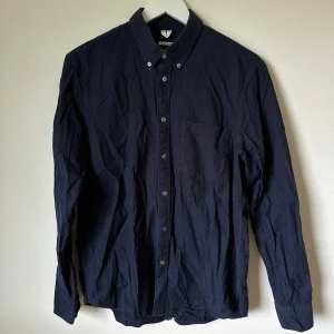 Mörkblå oxfordskjorta från Arket - Klassisk mörkblå oxfordskjorta från Arket i ekologisk bomull. Skjortan har button-down krage, bröstficka och knäppning framtill. Regular fit med långa ärmar och stilren look, perfekt till jeans eller chinos. 1F12