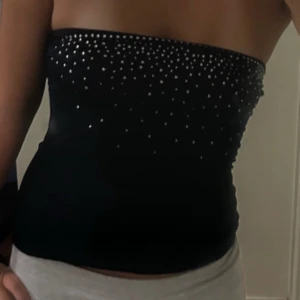 Blå tubtopp med glittriga detaljer - Snygg svart tubtopp med glittrande paljettdetaljer upptill. Perfekt för dig som vill sticka ut och addera lite extra bling till outfiten. Toppen är axelbandslös och sitter tight mot kroppen för en cool look.