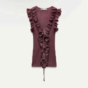 Vinröd volangtopp med knyt - Säljer denna supersöta vinröd/ lila topp med djup v-ringning, volangdetaljer längs axlar och fram, samt knyt framtill från Zara. Ärmlös och figurnära i passformen.