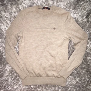 Beige merinoullströja från Morris - Snygg beige tröja från Morris i merinoull. Klassisk rund halsringning och diskret logga broderad på bröstet. Långärmad modell med ribbade muddar och nederkant. Perfekt för lager-på-lager och stilren look. Kom privat för mer info och pris!