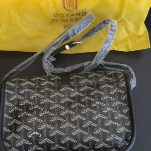 Svart axelväska - Säljer en snygg svart axelväska från G-yard med deras ikoniska mönster i vitt och grått. Väskan har justerbar axelrem och klassisk silvrig spänndetalj framtill. Perfekt för dig som vill ha en stilren och trendig accessoar med lyxig känsla.