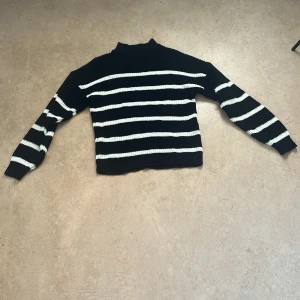 Svartvit randig stickad tröja - Säljer en svart stickad tröja med vita horisontella ränder. Tröjan har långärmade och en lite högre hals. Materialet är grovstickat och känns mjukt och skönt mot huden. Perfekt för dig som gillar klassisk stil med en twist. Aldrig använd, pris kan diskuteras 
