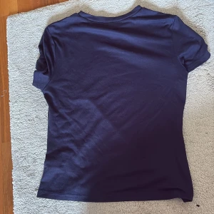 Mörkblå basic t-shirt - En enkel och stilren mörkblå t-shirt med rund hals och korta ärmar. Modellen är klassisk och passar perfekt till jeans eller shorts. Materialet känns mjukt och skönt mot huden, troligtvis bomull eller en bomullsblandning. Perfekt för dig som gillar minimalistisk stil.