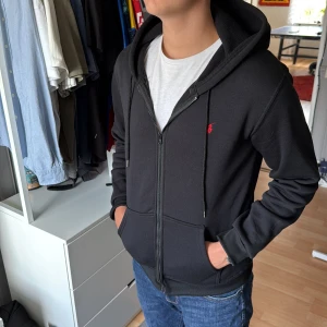Svart hoodie från Polo Ralph Lauren - Svart hoodie från Polo Ralph Lauren med dragkedja och huva. Klassisk röd broderad logga på bröstet, snörning i huvan och två fickor framtill. Storlek M! skriv för funderingar 😄