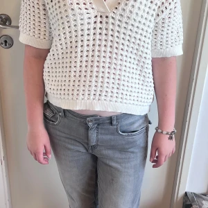 Vit stickad kortärmad tröja - Vit stickad tröja med korta ärmar och v-ringning. Tröjan har ett luftigt, hålmönstrat stickat material och ribbade muddar vid ärmslut och nederkant. Perfekt för lager-på-lager och en chill, trendig look.