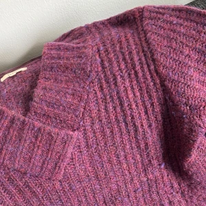 Vinröd stickad v-ringad tröja Verse - Mysig vinröd stickad tröja från Verse med v-ringning och breda ribbade muddar. Tröjan har lång ärm och en chunky känsla, perfekt för kyliga dagar. Färgen har inslag av lila och rosa toner för en unik look.