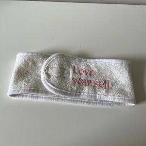 Vitt hårband  - Säljer ett vitt hårband i mjuk frotté med broderad texten 'Love yourself.' i rosa framtill. Diademet har kardborreknäppning för enkel justering och passar perfekt för att hålla håret borta vid hudvård eller sminkning.