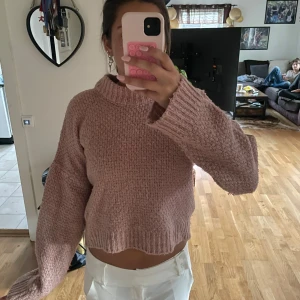 Rosa stickad tröja från NA-KD - Mysig rosa stickad tröja från NA-KD med grov struktur och ribbade muddar. Tröjan har en hög krage och är lite croppad i modellen. Perfekt för lager-på-lager och chill dagar.