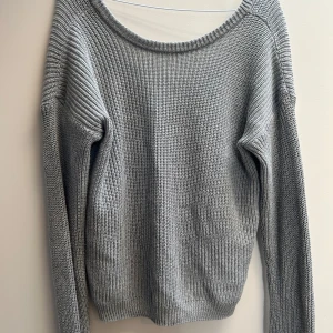 Grå stickad tröja off shoulder - En enkel och stilren grå stickad tröja med rund halsringning och långa ärmar. Perfekt för lager-på-lager och passar till både jeans och kjol. Tröjan har en klassisk passform och är riktigt skön att bära under kyligare dagar. är en xxs men känns större