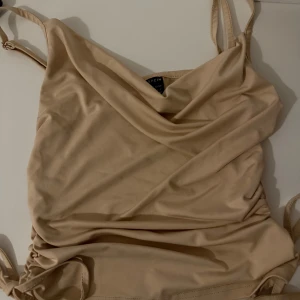 Beige linne  - Snygg beige linne från SHEIN med omlott-detalj och tunna axelband. Linnet har en draperad front och justerbara band i sidorna för en trendig look. Perfekt för dig som gillar stilrena och enkla plagg med en twist.