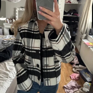 Kappa - Säljer en snygg rutig jacka från Zara i svart och vitt. Jackan har stora knappar framtill, klassisk krage och raka ärmar. Perfekt att slänga över en hoodie eller t-shirt för en chill look.