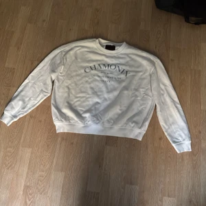 Vit sweatshirt Chamonix från 157 - Vit sweatshirt från 157 i storlek M med trycket 'CHAMONIX Mont Blanc Auvergne-Rhone-Alpes France' i blått på bröstet. Tröjan har rund hals, långa ärmar och ribbade muddar. Mjuk insida och klassisk passform, perfekt för chill dagar.