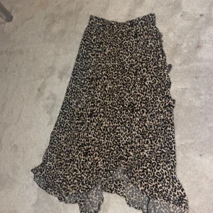 Leopardmönstrad volangkjol - Snygg långkjol med leopardmönster och volangdetaljer. Kjolen har en asymmetrisk nederkant och är i tunnt, flowy material som ger en cool vibe. Perfekt för dig som vill sticka ut lite extra.
