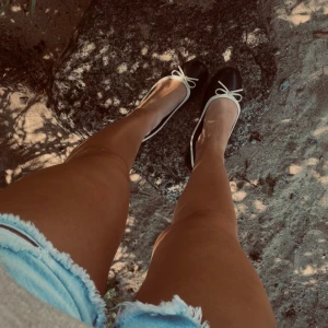 Svarta ballerinaskor med rosett - Snygga svarta ballerinaskor med vit kant och söt rosett framtill. Skorna har rund tå och platt sula, perfekta för en avslappnad och trendig look. Passar perfekt till shorts eller klänning under varma dagar.