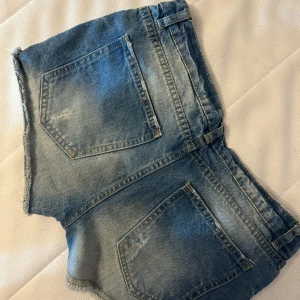 Blå slitna jeansshorts från Pull&Bear - Snygga blå jeansshorts från Pull&Bear med slitna detaljer och fransig kant. Klassisk femficksmodell med låg midja och dragkedja. Tyvärr för små för mig därför jag säljer de, super coola!