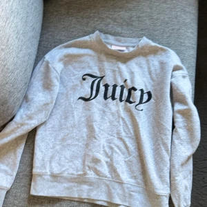 Grå sweatshirt Juicy Couture XXS - Supermjuk grå sweatshirt från Juicy Couture med svart tryck 'Juicy' på bröstet. Klassisk crewneck-modell med långa ärmar och relaxed fit. Perfekt för en chill och trendig look.