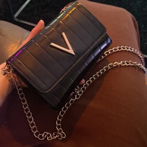 Svart axelväska med kedja och V-detalj - Snygg svart axelväska från Valentino med glansig finish och guldkedja. Köpt för ca 1.5 - 2 år sedan. Nypris ca 700-800 kr 