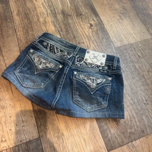 Miss Me shorts  strl 26 - Snygga mörkblå jeansshorts från Miss Me med blingade detaljer och broderier på bakfickorna. Klassisk femficksmodell med slitningar och dekorativa nitar. Perfekta för dig som vill sticka ut med coola detaljer och en edgy look. Skulle säga storlek XS-S. Hör av er om ni vill se hur de sitter på. y2k
