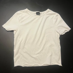 Vit basic t-shirt från Gina Tricot - Enkel och stilren vit t-shirt från Gina Tricot med rund halsringning och korta ärmar. Tillverkad i mjuk bomull som känns skön mot huden. Perfekt att matcha med jeans eller kjol för en clean look.