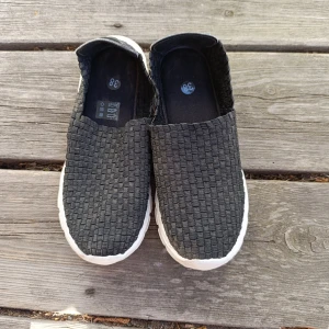 Svarta slip-on sneakers flätad look, storlek 38 - Svarta slip-on sneakers med flätad ovandel och vit, chunky sula. Skorna har en rund tå och är tillverkade i syntetmaterial. Perfekta för dig som gillar en clean och sportig stil med en twist.