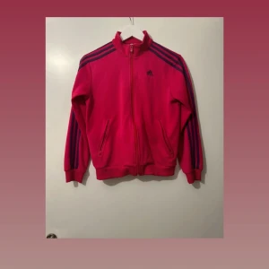 Rosa Adidas kofta - Storlek M - Säljer en snygg rosa Adidas kofta i storlek M. Den är använd några gånger men mycket bra skick utan synliga defekter. Koftan har en dragkedja framtill, sidfickor och Adidas logotypen på bröstet. Materialet är mjukt och bekvämt.