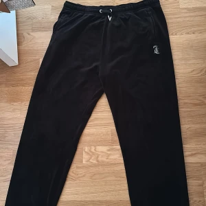 Svarta Juicy Couture mjukisbyxor - Svarta mjukisbyxor från Juicy Couture i mjuk sammet med dragsko i midjan. Klassisk Juicy-logga i strass på baksidan och liten broderad logga fram. Perfekta för en chill och trendig look. (Mudd längst ner)