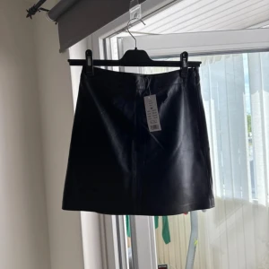 Svart skinnkjol från Gina Tricot - Snygg svart skinnkjol från Gina Tricot med A linje passform. Kjolen är kort och har en stilren look som passar perfekt till sneakers eller boots. Materialet är skinn och ger en cool vibe till outfiten. Perfekt för dig som vill ha en edgy touch på din stil.