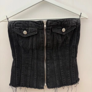 Jeans topp - Cool svart korsettopp i jeansmaterial med dragkedja framtill och fransiga kanter nertill. Baksidan har smock för extra stretch och passform. Från Zara i storlek S
