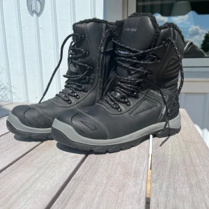 Svarta vinterkängor från Blåkläder - Säljer ett par oanvända rejäla svarta arbets-vinterkängor från Blåkläder med stålhätta, grov sula, snörning och dragkedja på sidan. Fodrade med mjukt material för extra värme och komfort. Perfekta för kalla dagar och tuffare väder. Helt oanvända, storlek 44 men passar för dom som har 43. Nypris: 2600kr, säljer för 1899kr. Finns i Bollebygd 