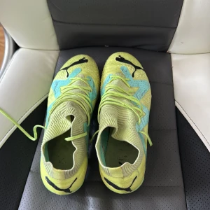 Puma gula fotbollsskor med snörning - Snygga fotbollsskor från Puma i ljusgul och mintgrön färg med blå detaljer. Skorna har stickad ovandel, snörning och klassisk Puma-logga. Perfekta för dig som vill sticka ut på planen med en modern och sportig look.