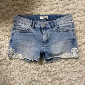Jeansshorts med spets - Snygga ljusblå jeansshorts från Lindex med vit  spetsdetalj. Storlek 146/152 = xxs/ xs 