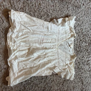 Vit blus med volang från Gina Tricot - Supersöt vit blus från Gina Tricot med volangdetaljer vid ärmarna och v-ringning. Blusen har broderade partier och är tillverkad i ett lätt och skönt material