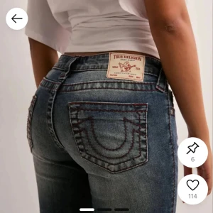 True Religion blå bootcut jeans - Snygga blå jeans från True Religion med ikoniska bakfickor och kontrastsömmar i rött. Modellen har bootcut-snitt och låg midja, tillverkade i klassiskt jeanstyg. Perfekta för dig som vill ha en cool och tidlös look.