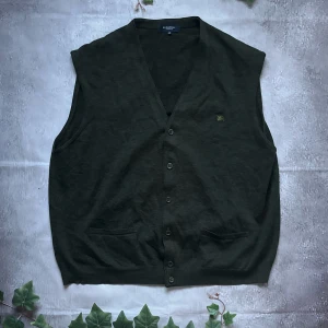 Burberry Merino Väst - Säljer denna fina och stiliga internationella Burberry västen för bara 599kr! Otroligt billigt pris för Burberry!  🎨 Färg: Mörkgrön 📏 Storlek: Burberry storlek 10 vilket motsvarar XL 📐 Mått: Längd - 68cm, Axelbredd - 48cm ♻️ Skick: 9/10 utan defekt eller fläckar på utsidan. Bara taggen är borttvättad  🧵 Material: 60% Lana Merino, 40% Acrilico  ‼️Skickas dagen efter köpet
