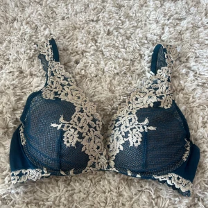 Blå spets-bh från Intimissimi - Supersnygg blå bh från Intimissimi med krämvit spets och blommiga broderier. Axelbanden är dekorerade med spets och bh:n har justerbara band samt hakknäppning bak. Perfekt för dig som gillar detaljer och vill ha något extra under kläderna.
