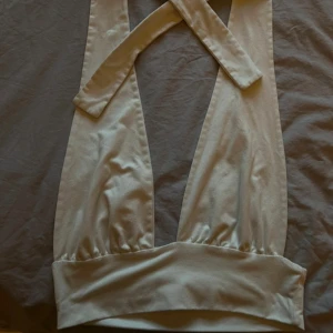 Beige omlott tubtopp med bred kant - Trendig vit  halterneck tröja. Toppen har bred band nedtill för en snygg passform och är tillverkad i ett mjukt, stretchigt material. Perfekt för dig som vill ha en stilren och modern look. Storlek M