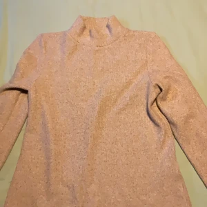 Beige polotröja från Amisu - Mysig beige polotröja från Amisu i storlek S. Tröjan är ribbstickad med hög krage och långa ärmar, perfekt för lager på lager under kyliga dagar. Enkel och stilren design som är lätt att matcha med olika outfits.