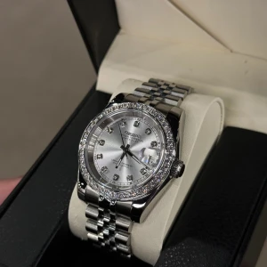 Seiko mod Datejust silver diamonds - Snygg Seiko Datejust med silverfärgad urtavla och länkarmband i rostfritt stål. Klockan har glittrande stenar runt boetten och som index, samt datumvisning med förstoringsglas. Klassisk och stilren design som sticker ut med sina detaljer.