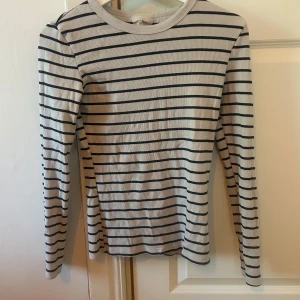 Randig långärmad tröja Gina Tricot - Säljer en vit långärmad tröja med svarta horisontella ränder från Gina Tricot, Basically Basics-kollektionen. Tröjan har rund halsringning och är i mjuk bomull, perfekt för en clean och enkel stil.