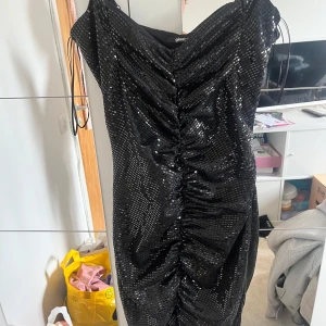 Svart glittrig klänning Gina Tricot - Snygg svart kortklänning från Gina Tricot med glittriga paljetter och rynkade detaljer framtill. 