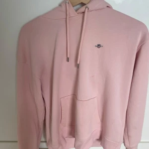 Ljusrosa hoodie från GANT i bomull - Säljer en ljusrosa hoodie från GANT i storlek S. Tröjan har huva med snörning, magficka och diskret GANT-logga broderad på bröstet. Tillverkad i mjuk bomull och har långa ärmar med ribbade muddar. Perfekt för en chill och avslappnad stil.jag köpte den i butik för 1400kr och den är oanvänd.färgen sälj inte i hemsidan. 