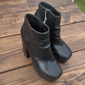 Svarta stövletter med klack från ASOS - Snygga svarta stövletter från ASOS med hög klack och rund tå. Skorna har dragkedja på insidan och är gjorda i ett slätt syntetmaterial som ger en clean look. Perfekta för dig som vill ha en stilren och edgy vibe till outfiten.